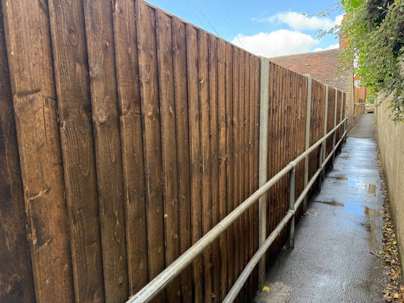 Tall dark stained closeboard fence running along an alleyway