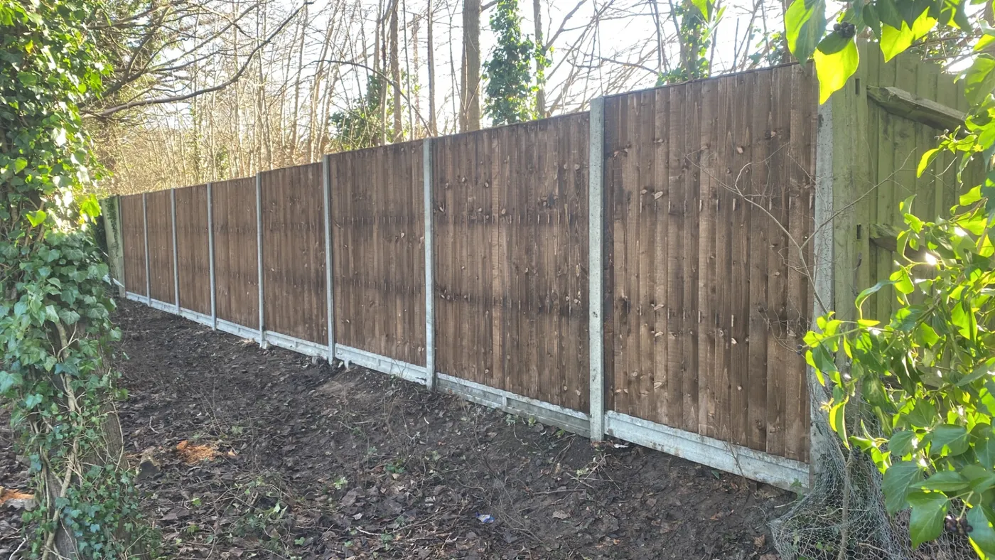 Long run of new dark stained fence panels along a woodland boundary