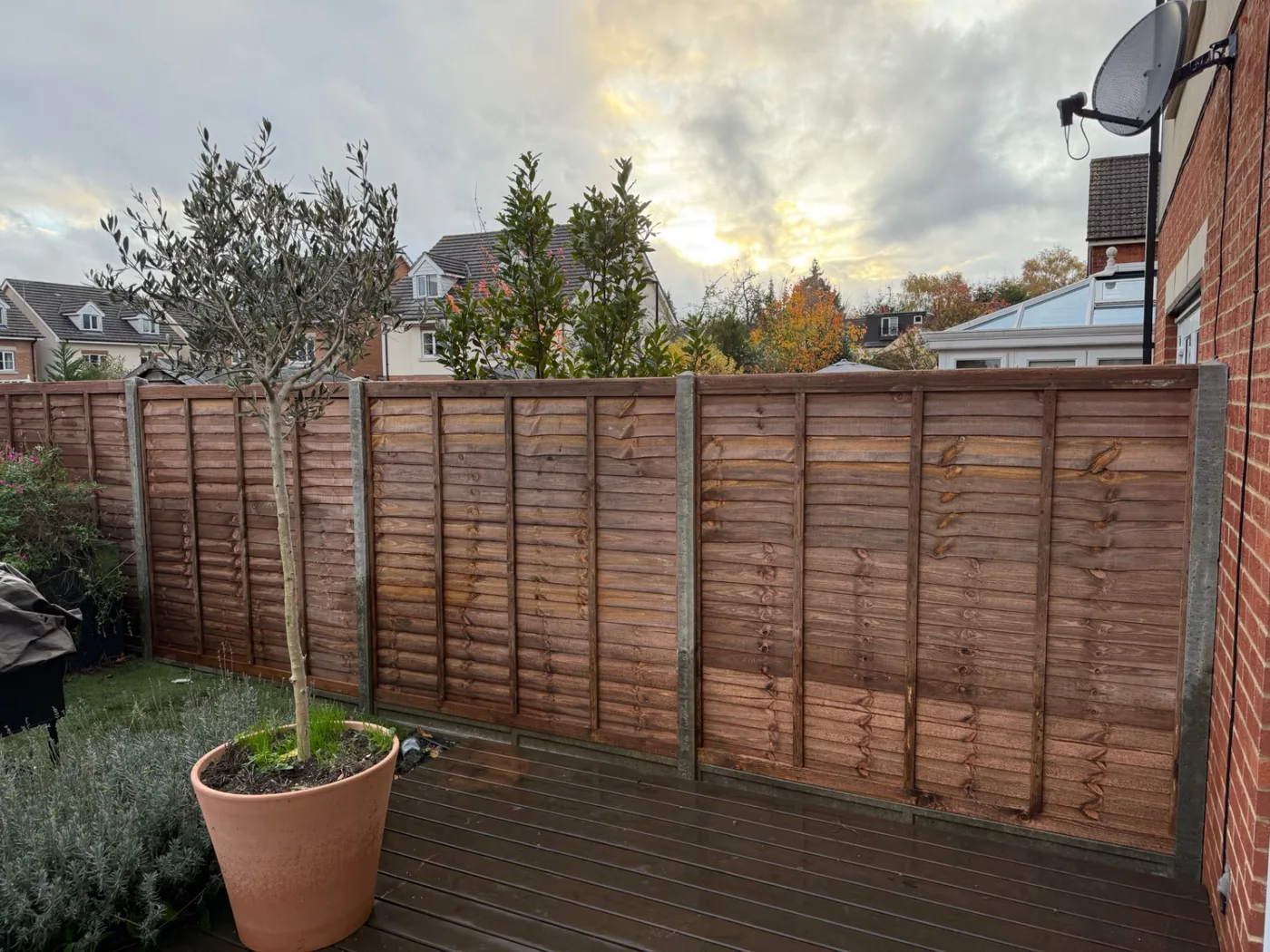 Brown lap fence panels with concrete posts beside a decked garden