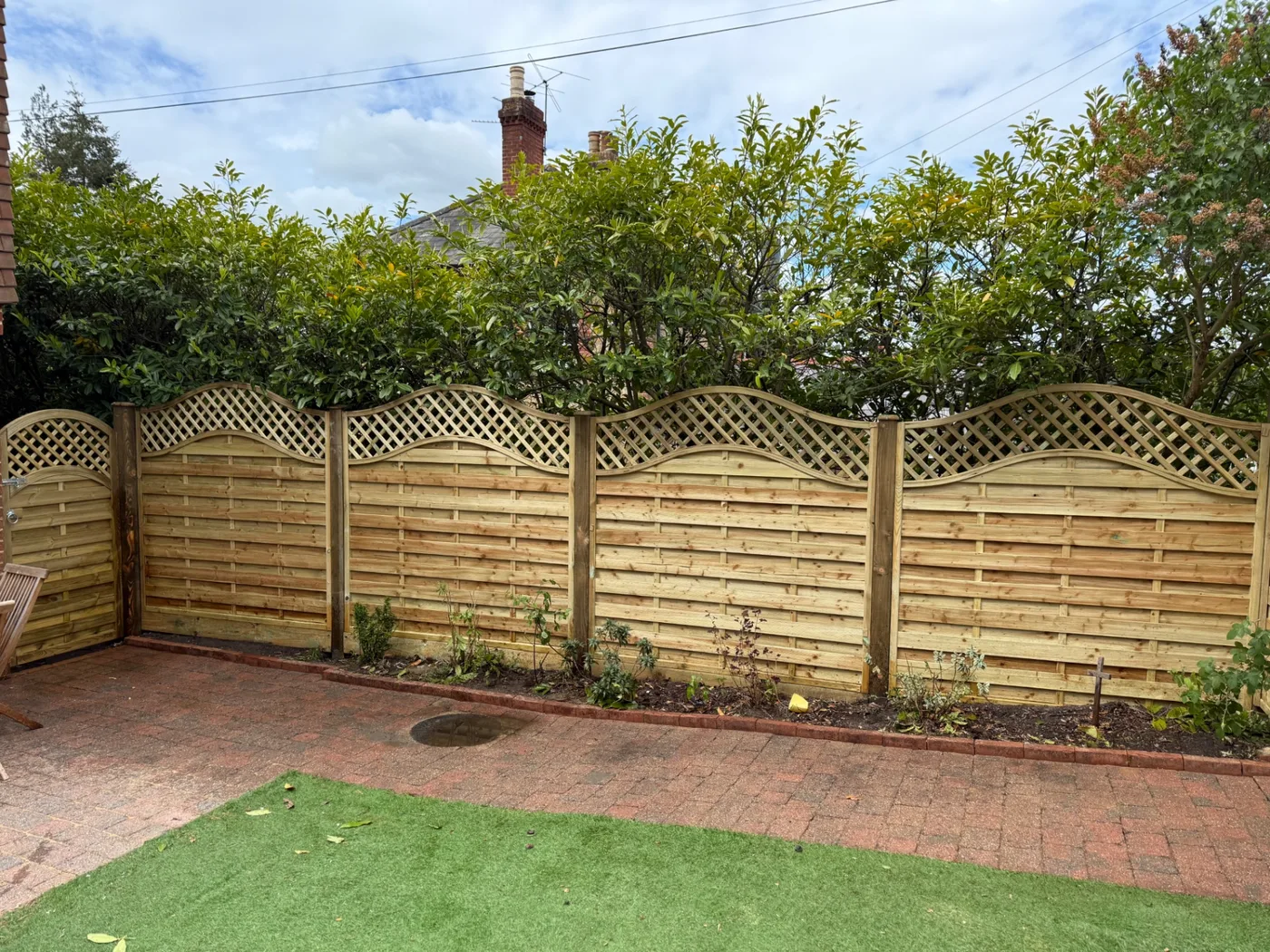 Decorative wave trellis topped fence panels between concrete posts
